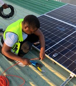 Technician working on solar panel installation with cables and tools on a sunny day.