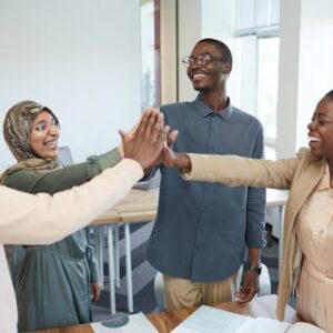 A joyful group of diverse colleagues high-fiving each other in an office, symbolizing teamwork and collaboration.