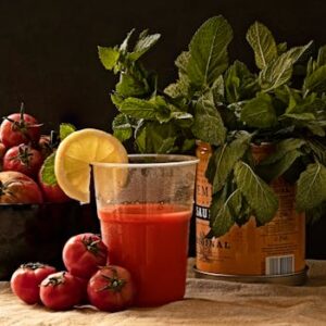 A refreshing glass of tomato juice with fresh basil, mint, and a slice of lemon on a rustic table.